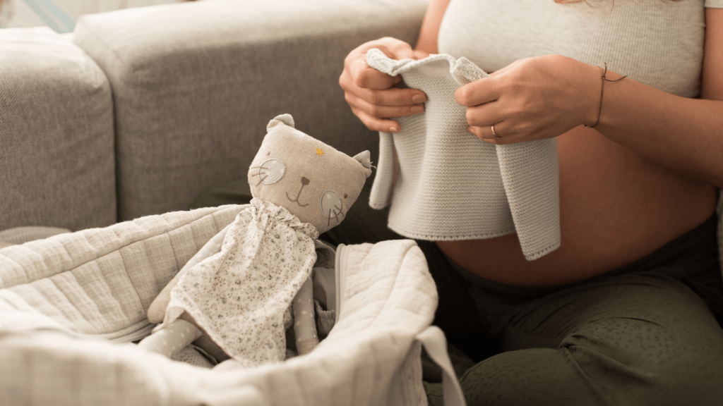 Pregnant woman packing a hospital bag with baby clothes and a soft toy